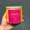Load image into Gallery viewer, Hand holding a candle labeled 'Mango & Coconut Milk' against a dark background