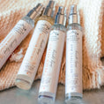 Load image into Gallery viewer, Five bottles of body spray on a textured surface with a woven mat in the background.
