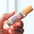 Load image into Gallery viewer, Hand holding a rollerball perfume bottle labeled 'Exotic Beach' against a light background