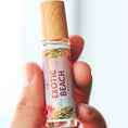 Load image into Gallery viewer, Hand holding a small bottle labeled 'Exotic Beach' against a light background