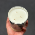 Load image into Gallery viewer, Hand holding a candle labeled 'Beach Breeze' against a dark background