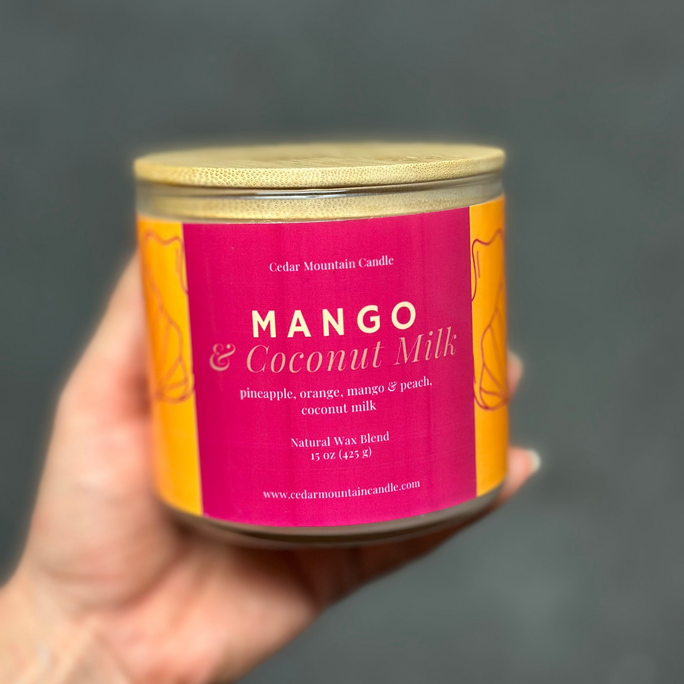 Hand holding a candle labeled 'Mango & Coconut Milk' against a dark background