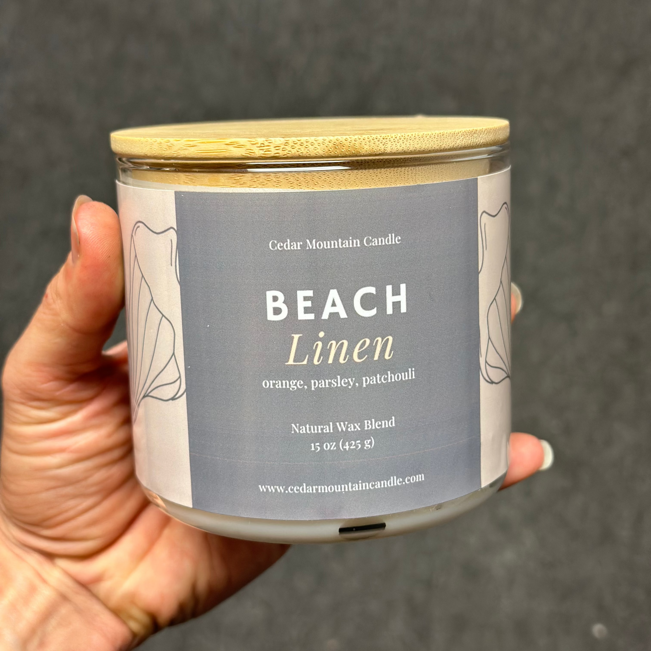 Candle jar labeled 'Beach Linen' held by a hand against a dark background