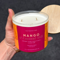Load image into Gallery viewer, Candle with 'Mango & Coconut Milk' label held by a hand against a dark background
