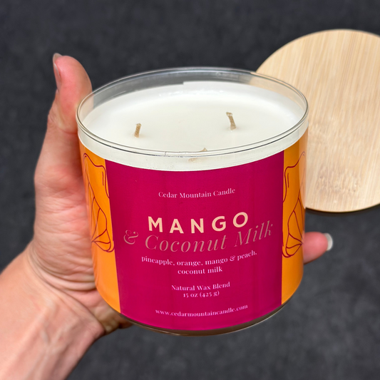 Candle with 'Mango & Coconut Milk' label held by a hand against a dark background