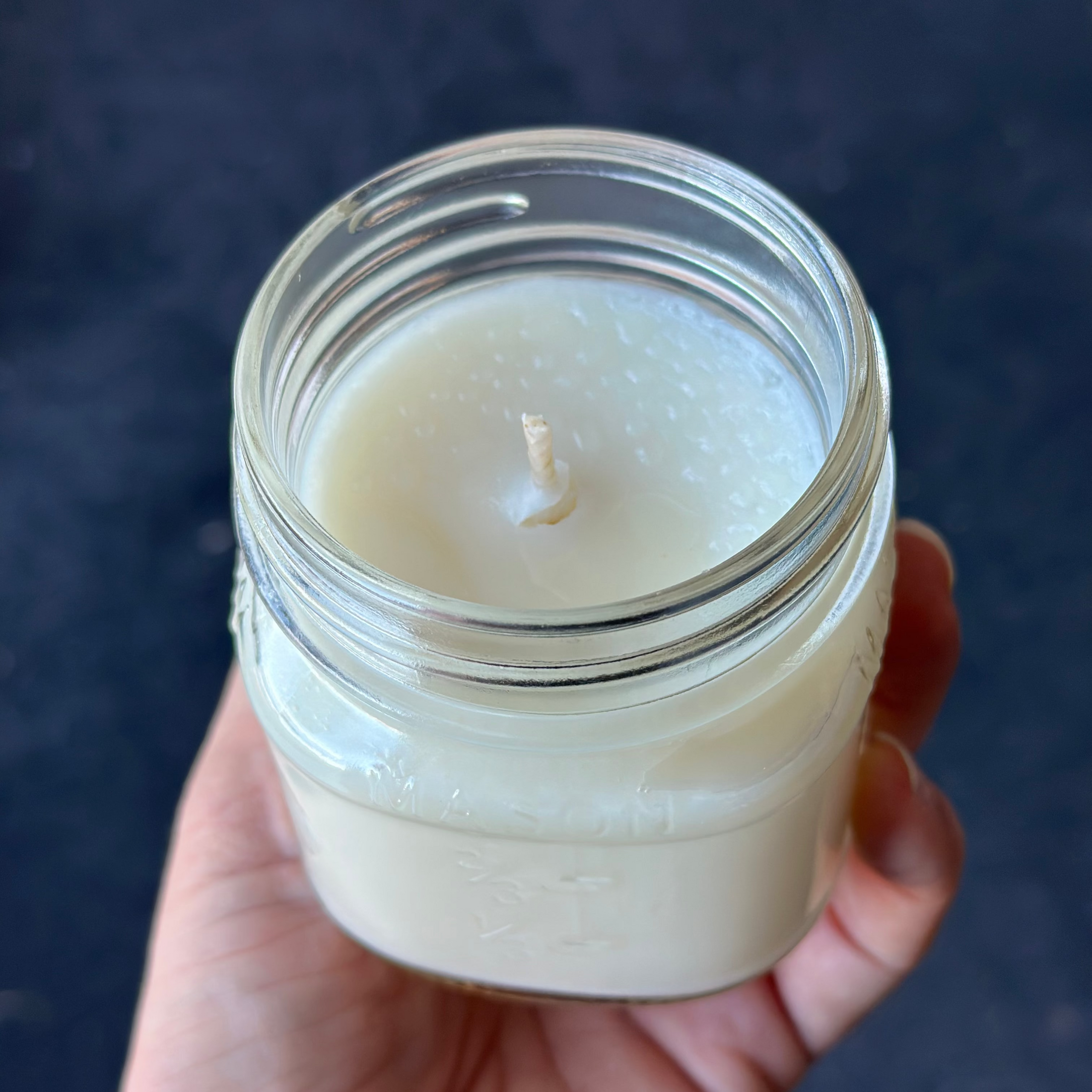 Hand holding a small glass jar with a candle against a dark background