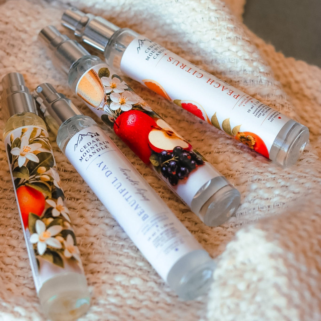 Three small bottles with floral and fruit designs on a textured fabric background