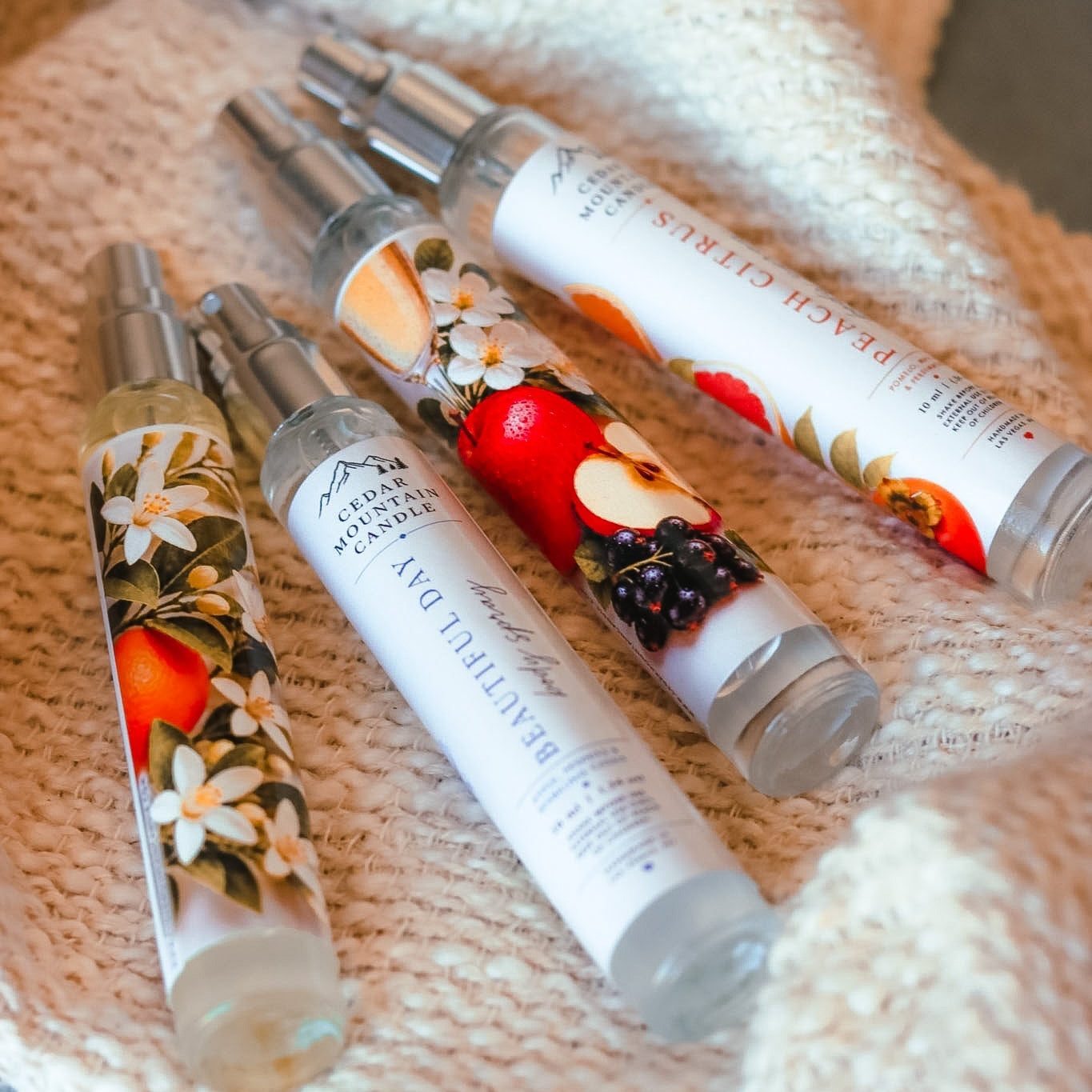 Three decorative glass bottles with floral and fruit designs on a textured fabric background