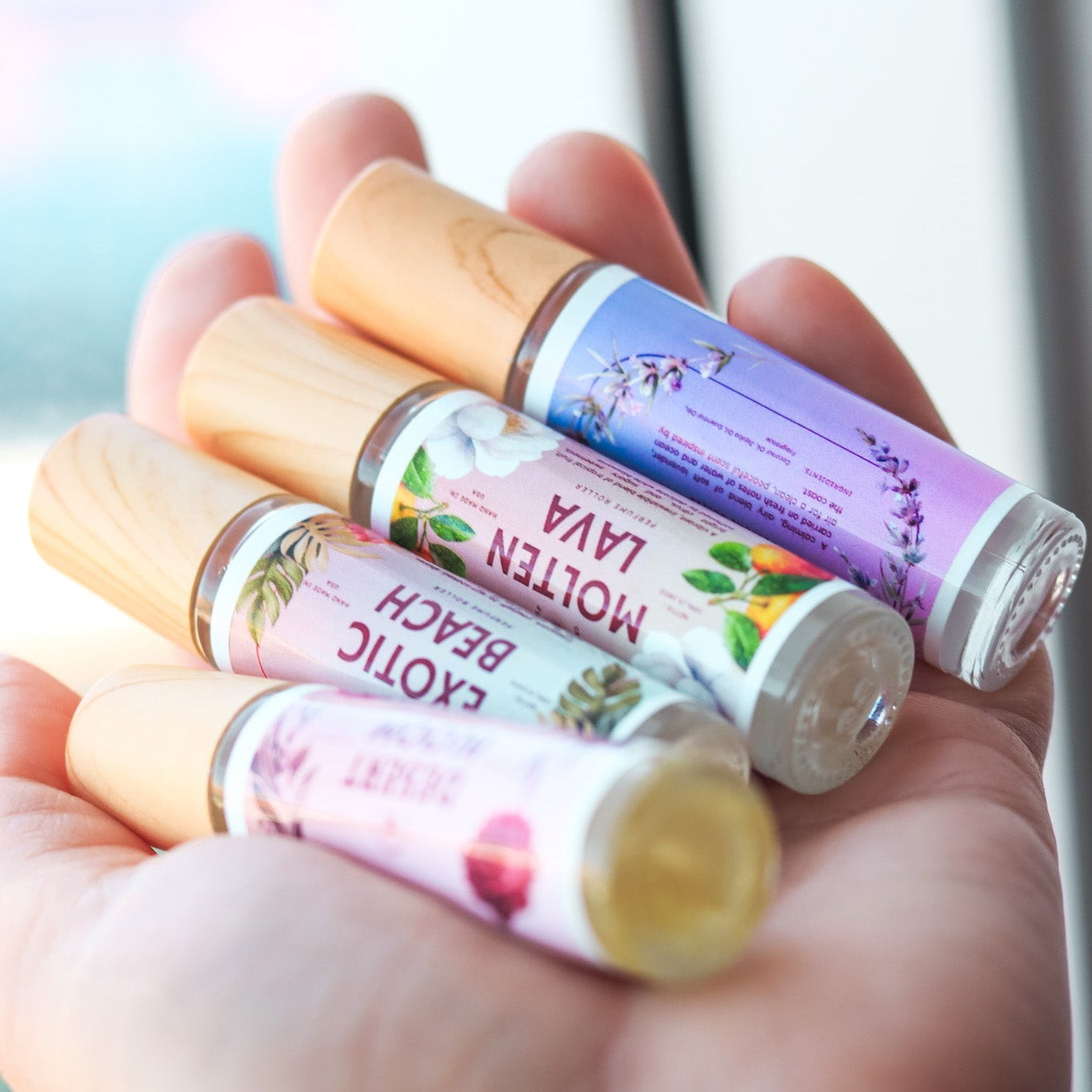 Hand holding four perfume rollerballs with colorful packaging against a blurred background