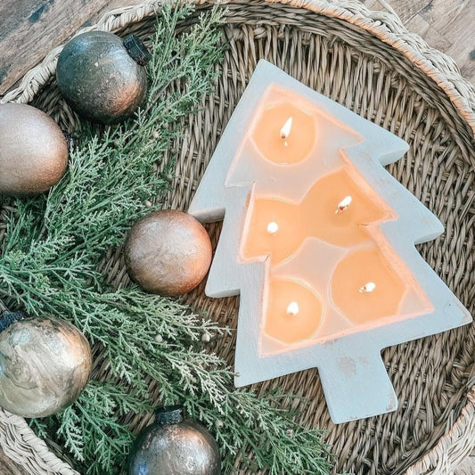 Christmas tree shaped candle burning on a rattan tray with Christmas ornament on it